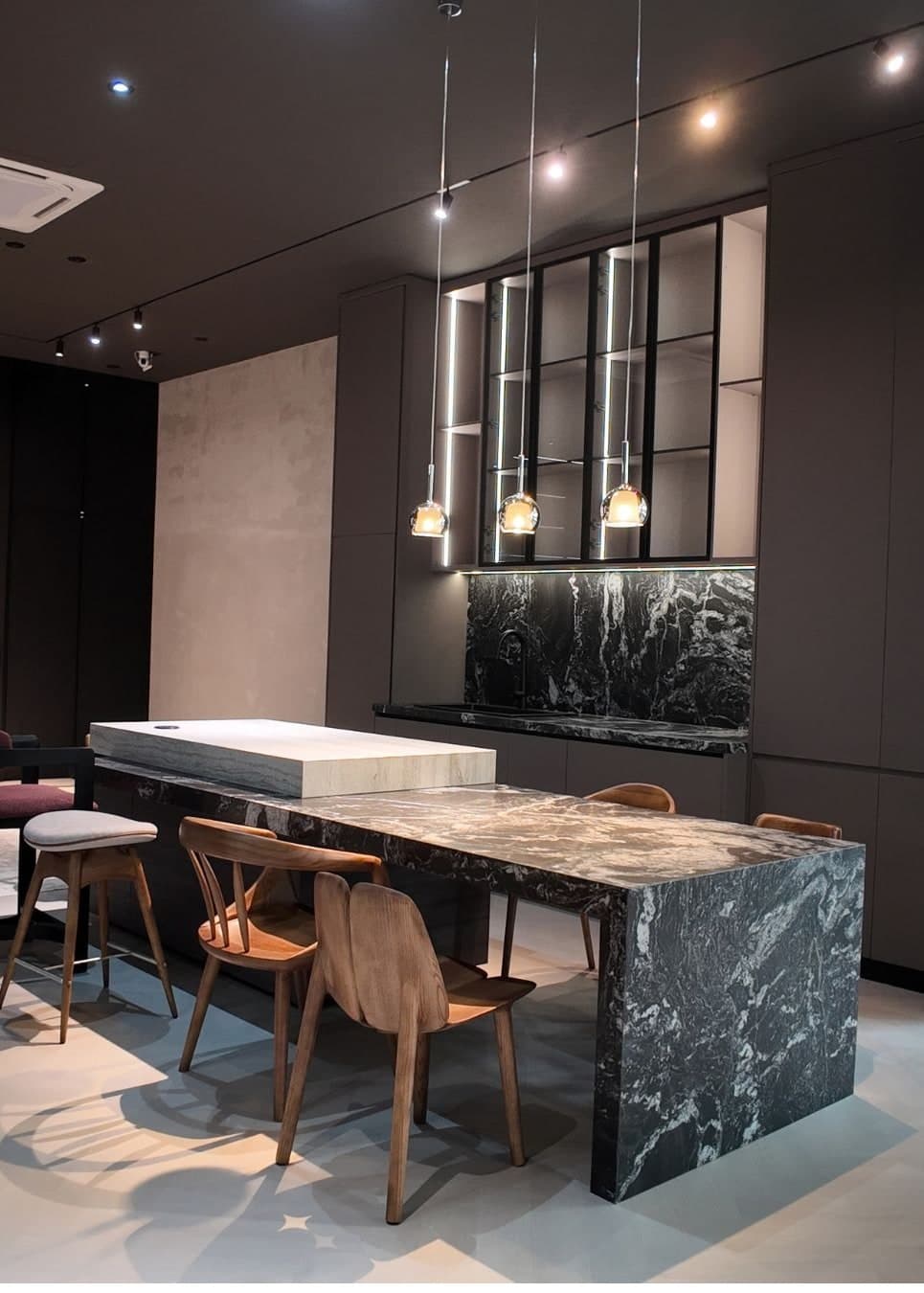 Black marble kitchen island and dining table with timber chairs under glass pendants